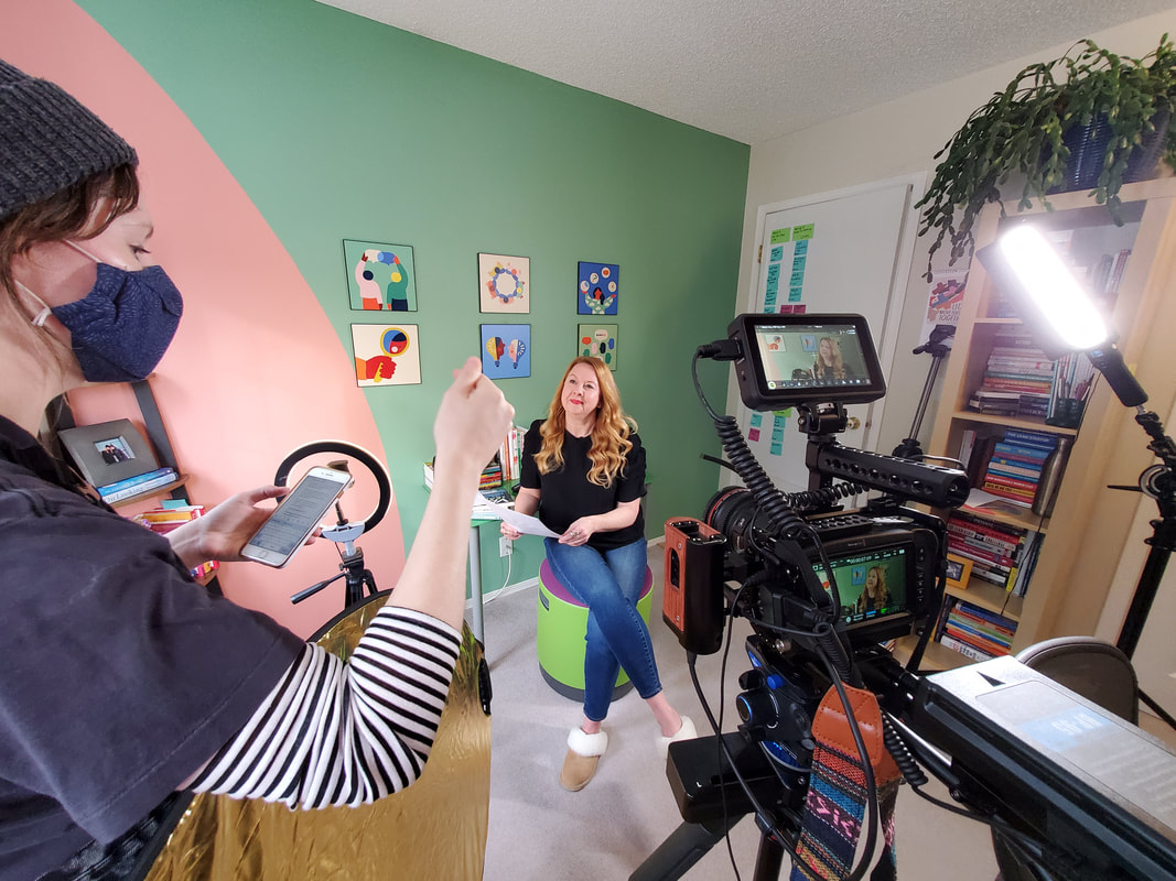 A woman is interviewed on camera in a bright and colourful office setting. She is looking at the producer.