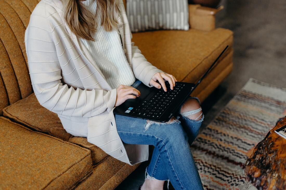 A woman sits on a couch while typing on a laptop