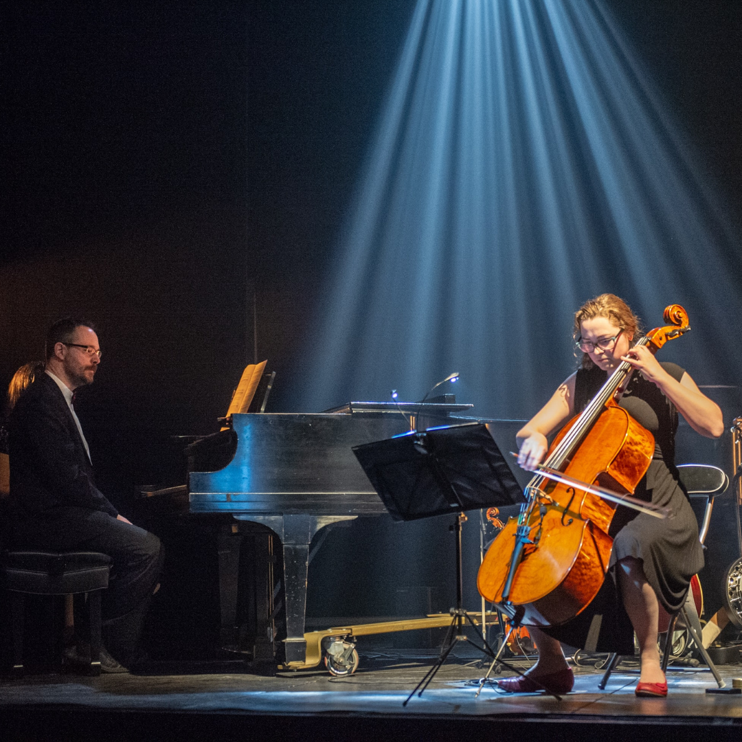 A woman plays the cello on stage. She is accompanied by a pianist.