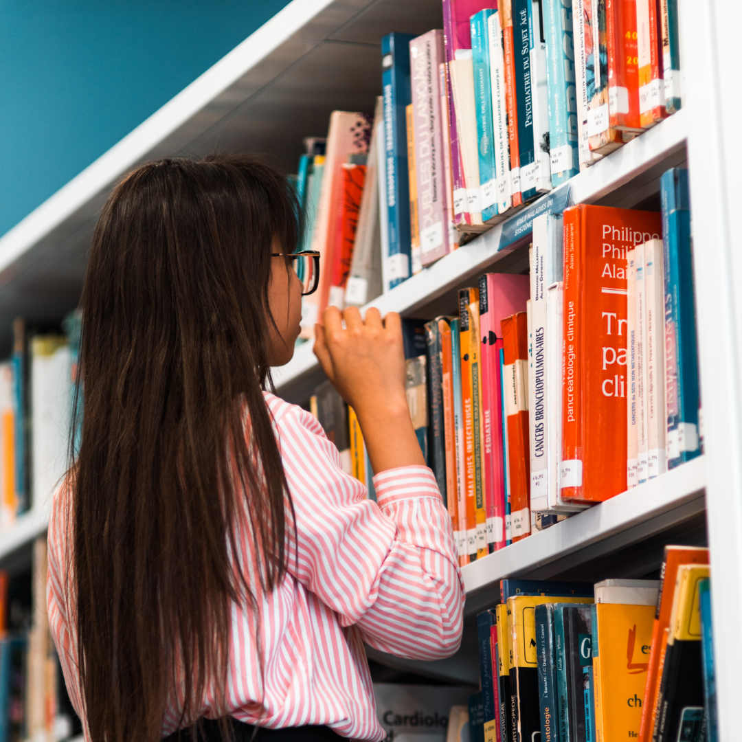 A young girl browses books on the shelves of a library. 
