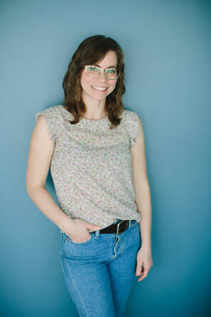 Jenny Spurr stands facing the camera. She is leaning against the wall with one hand in her pocket.